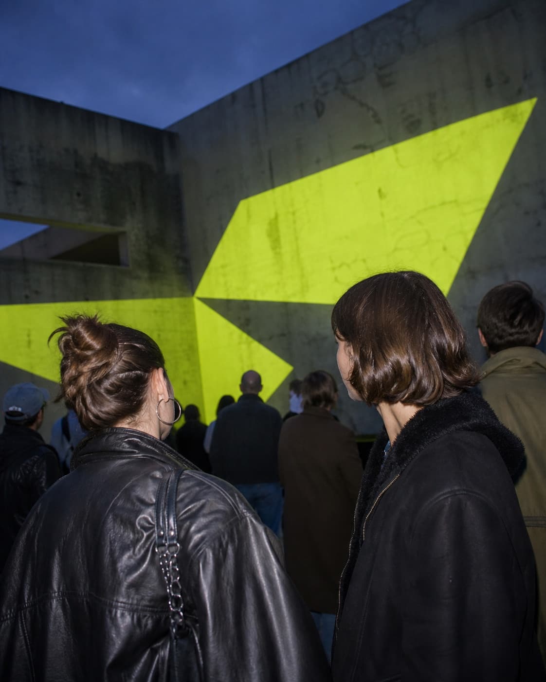 Visitors watching a chartreuse light installation in a concrete courtyard